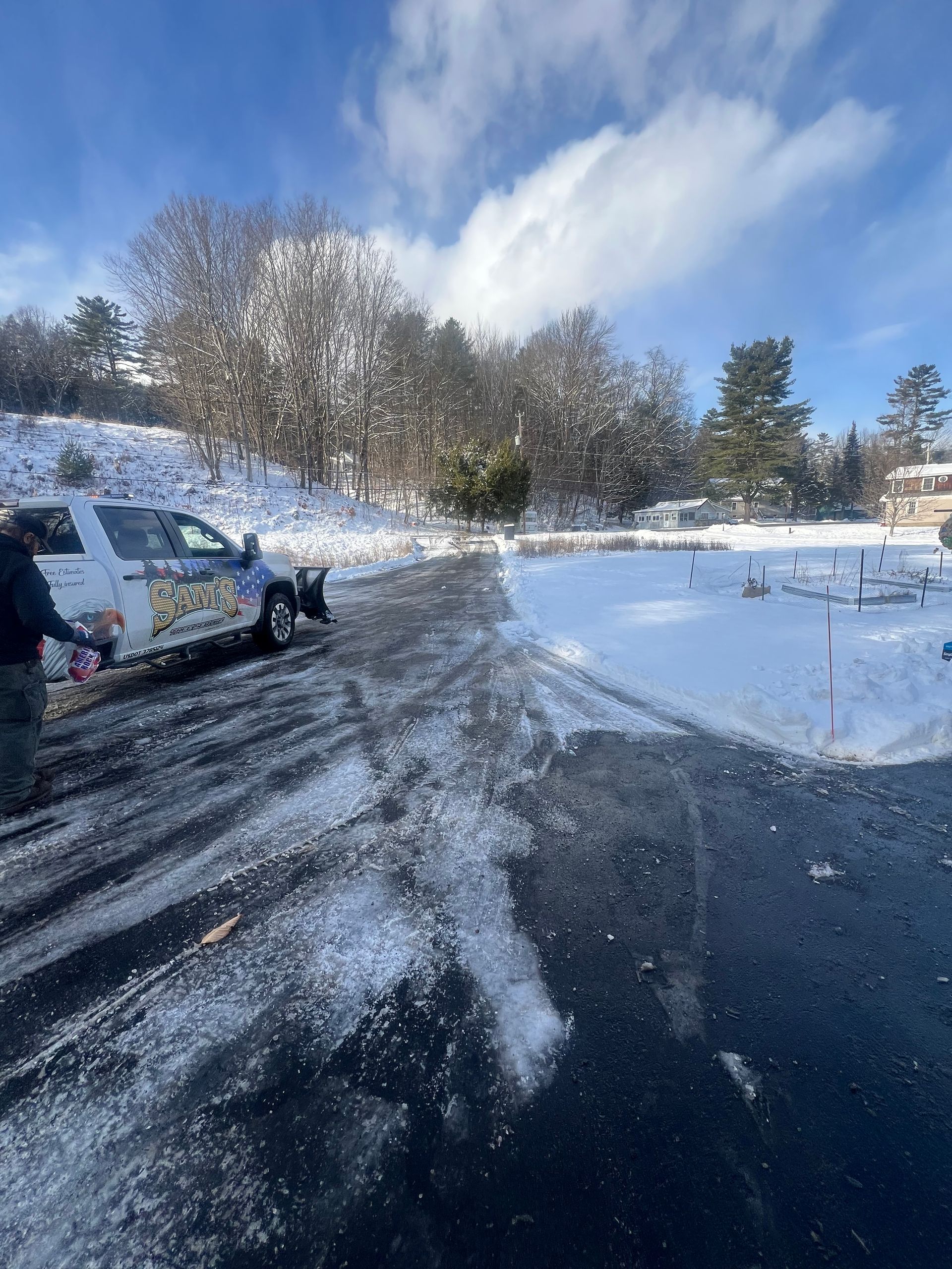 Snowy parking lot with a white van, plowed road, and bare trees under a blue sky