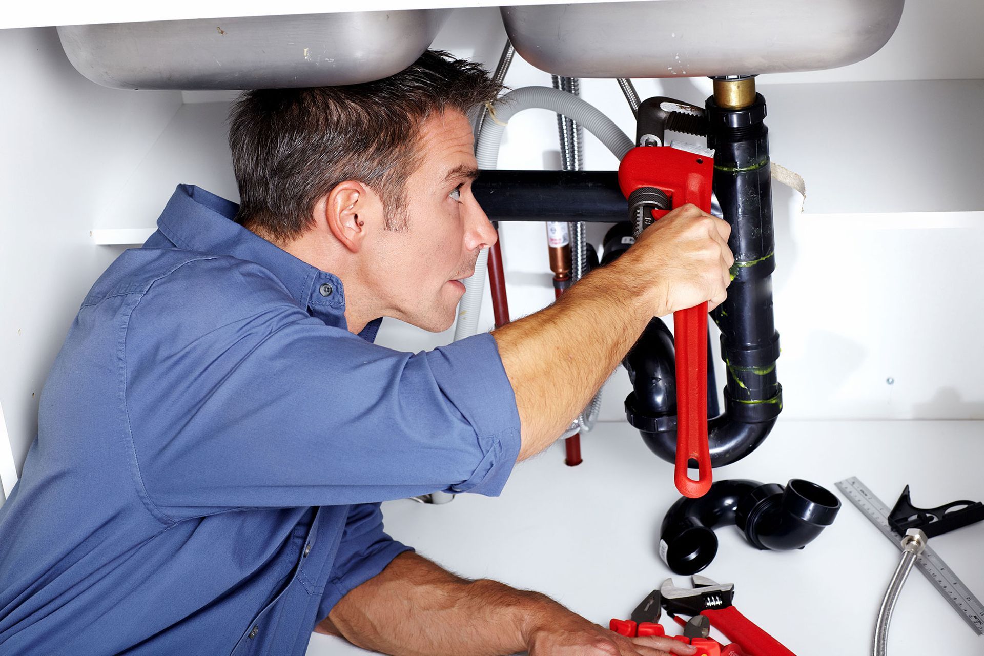 Plumber using a red pipe wrench to repair under-sink plumbing beneath a bathroom sink