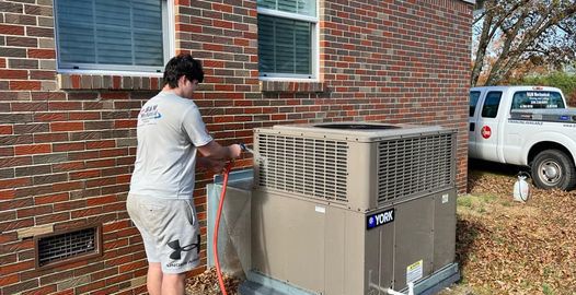 A man is working on an air conditioner outside of a brick house.