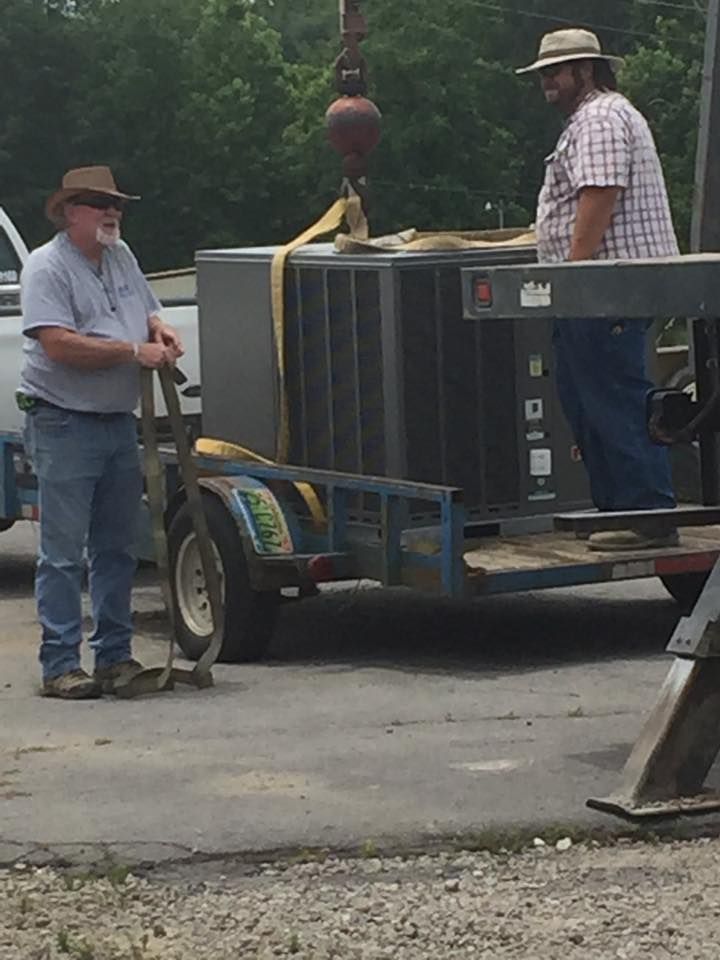 Two men are standing next to a trailer with a large appliance on it.