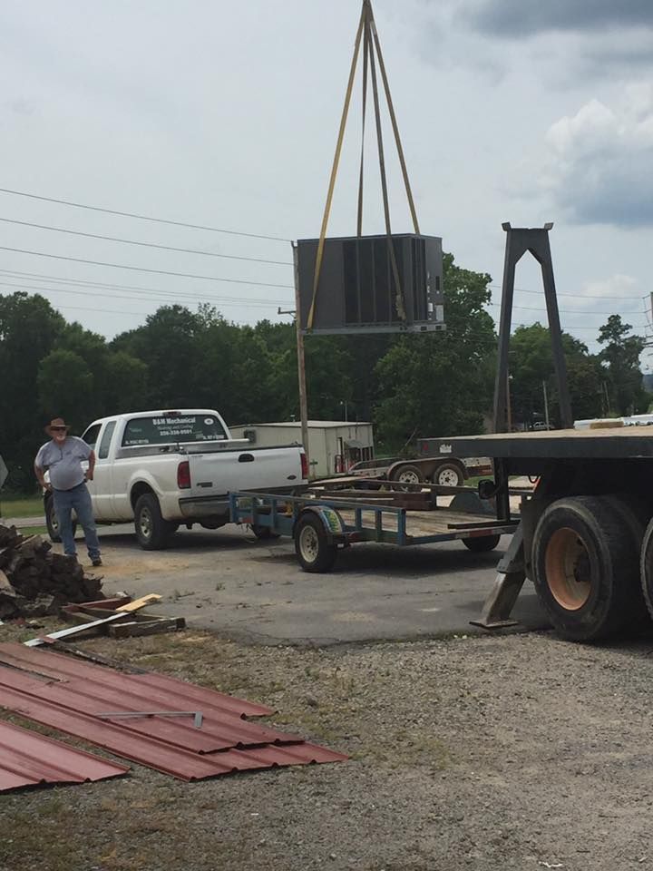 A man is standing next to a truck that is carrying a crane.