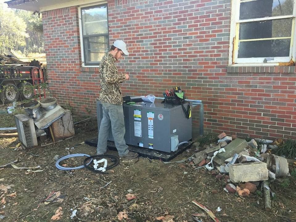 A man is working on an air conditioner outside of a brick house.