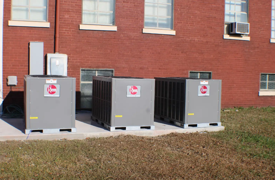 Three air conditioners are lined up in front of a brick building.
