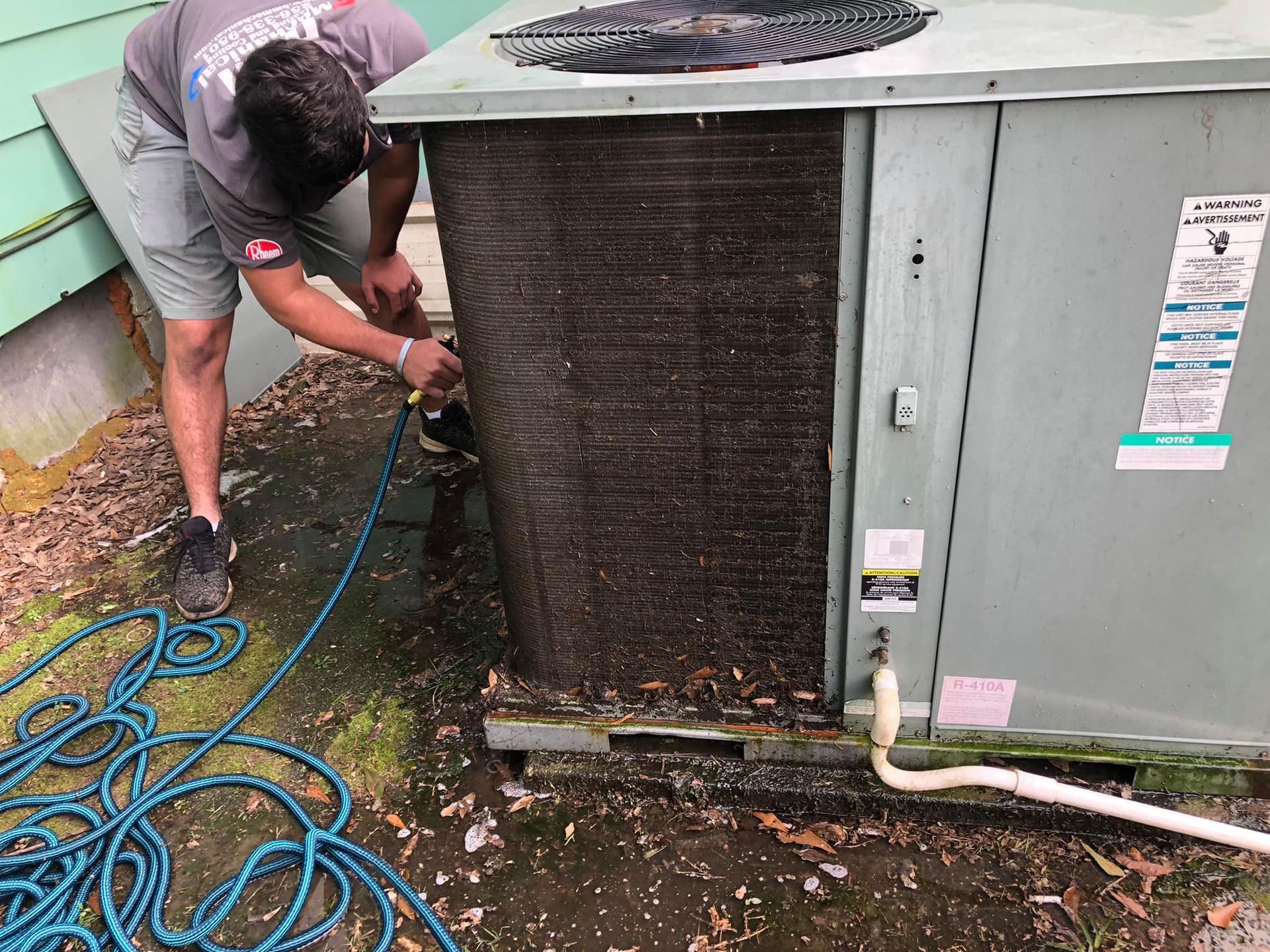A man is working on an air conditioner outside of a house.