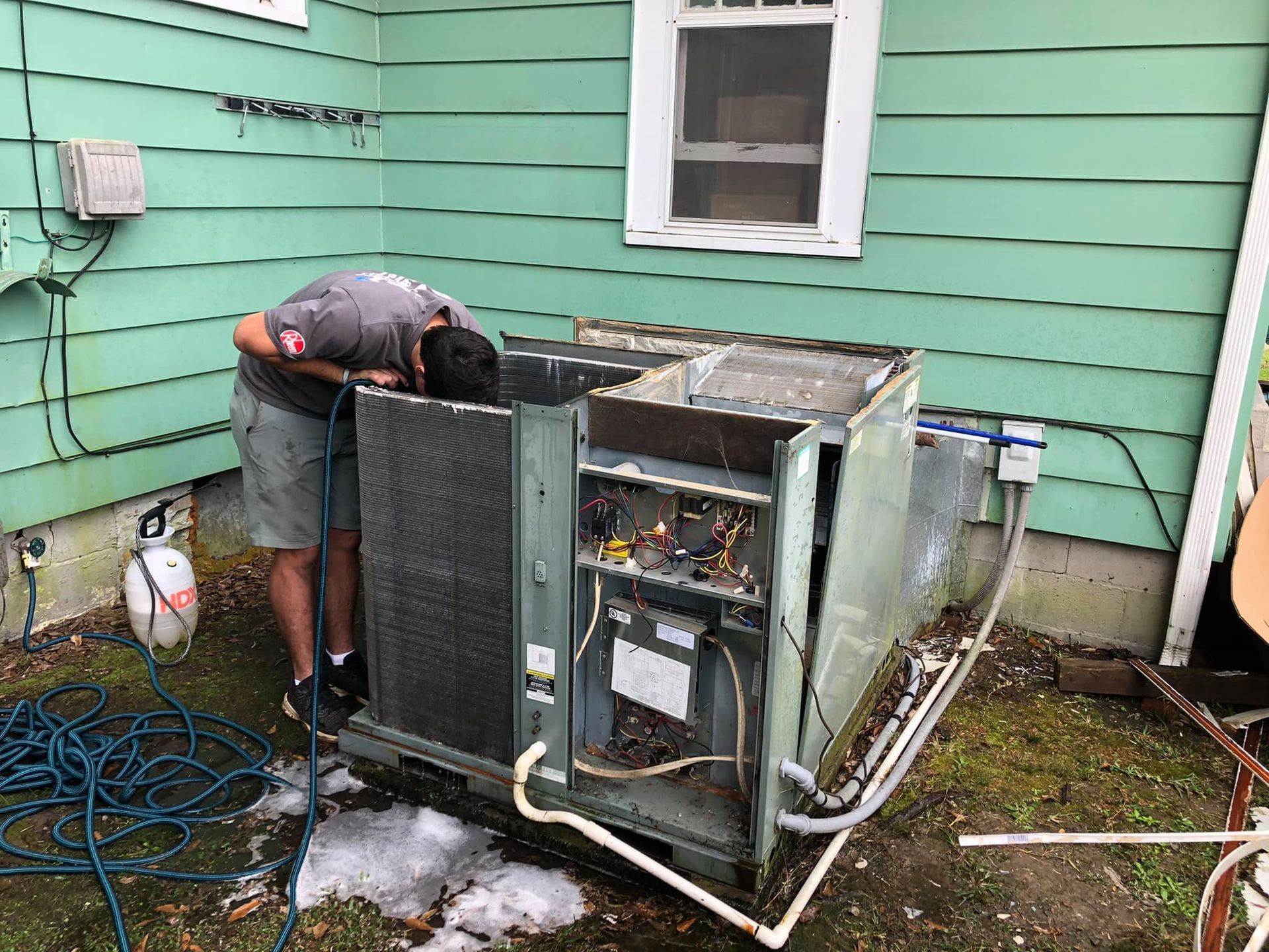 A man is working on an air conditioner outside of a house.