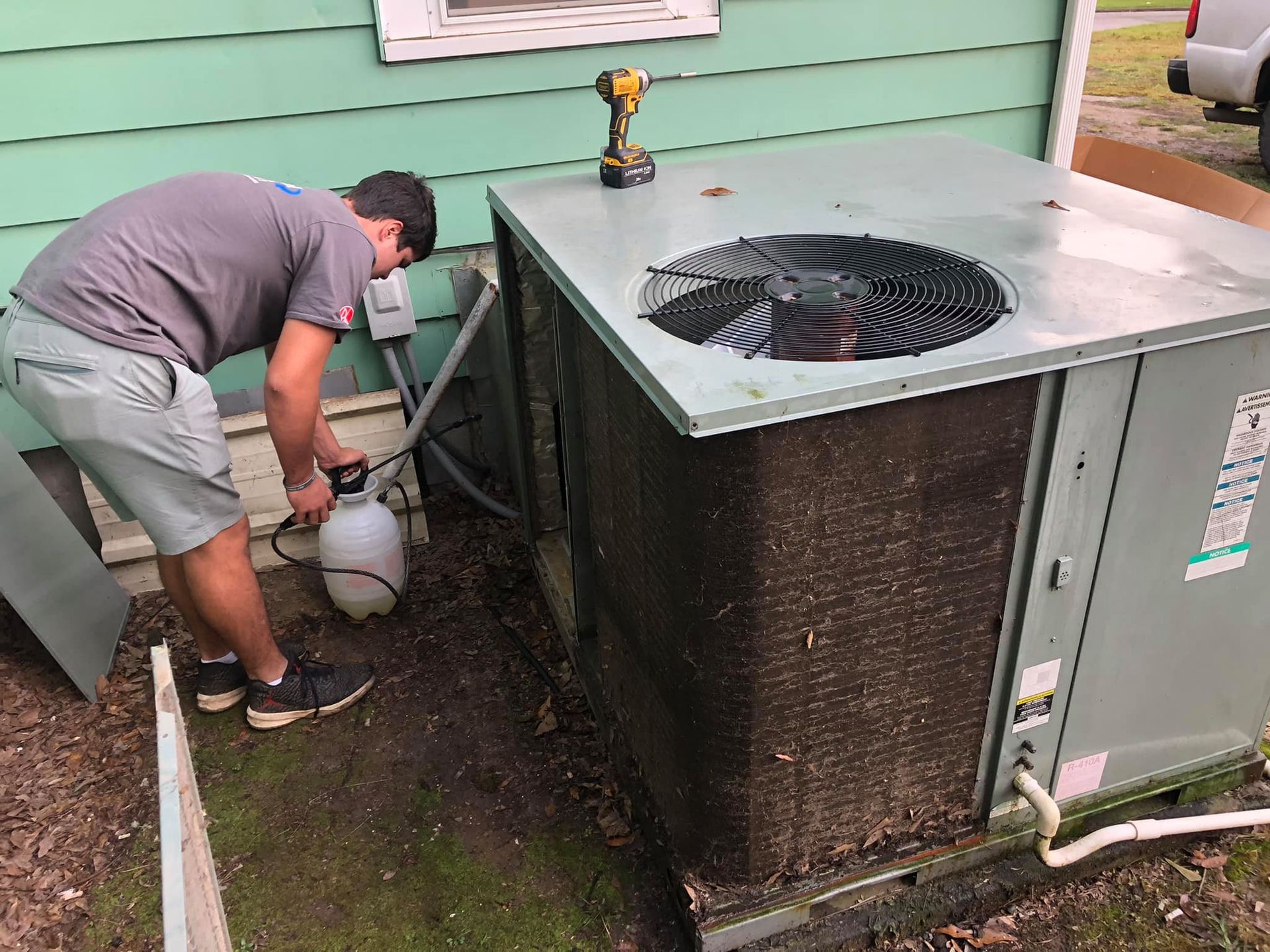 A man is cleaning an air conditioner outside of a house.