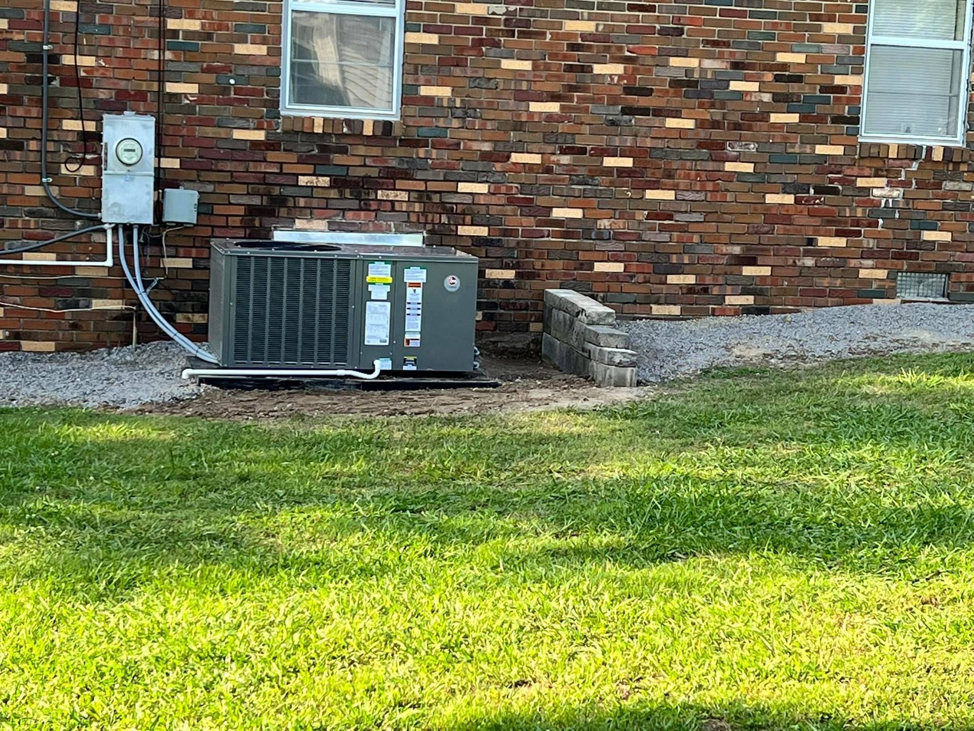 An air conditioner is sitting in the grass in front of a brick building.