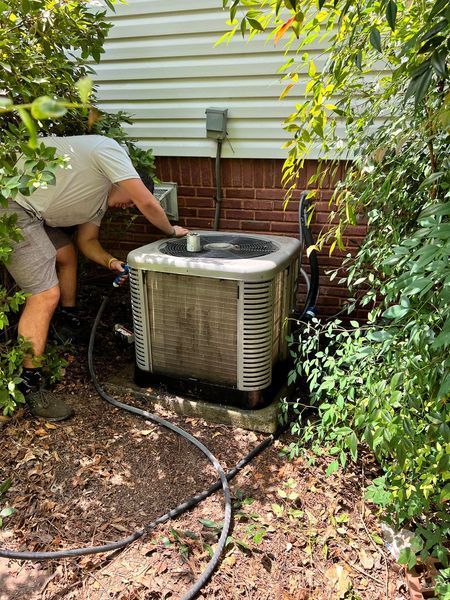 A man is working on an air conditioner outside of a house.