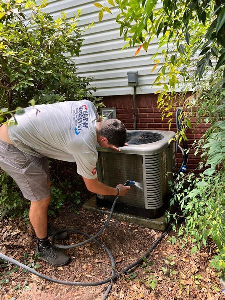 A man is cleaning an air conditioner with a hose.