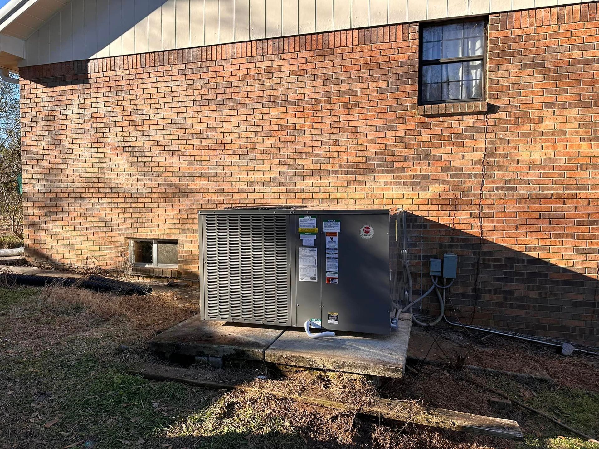 An air conditioner is sitting on the side of a brick building.