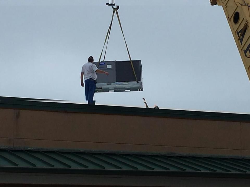 A man is standing on the roof of a building lifting something.