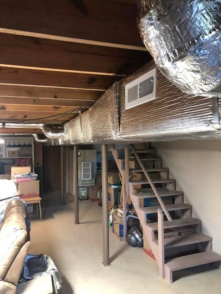 A basement with stairs, duct, and a couch in it.