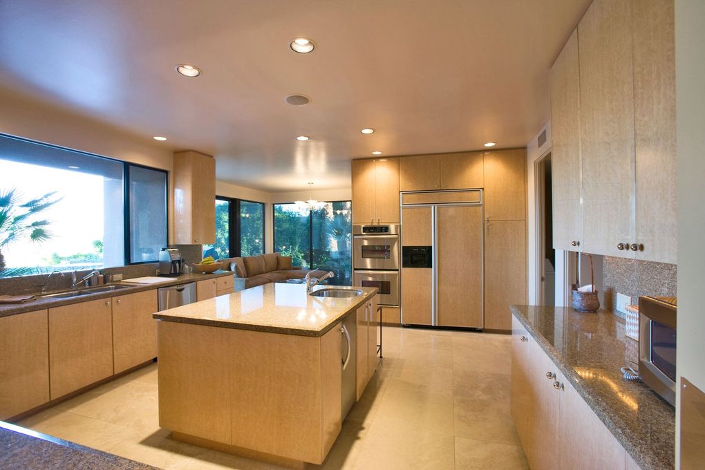 Modern kitchen with large island, stainless steel refrigerator, wood cabinets, and bright recessed lighting