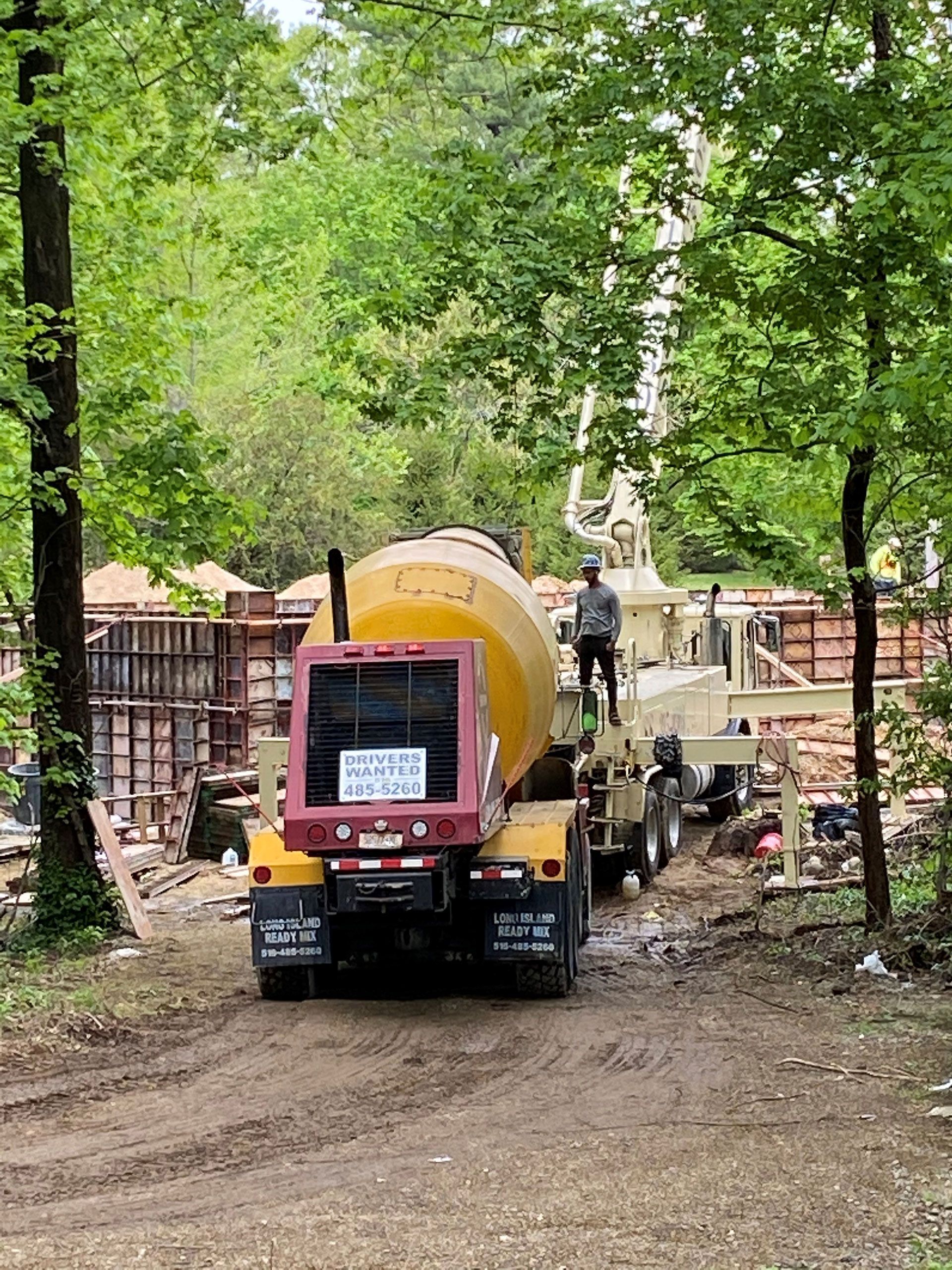 Concrete mixer truck on a dirt road in a wooded area with a worker.