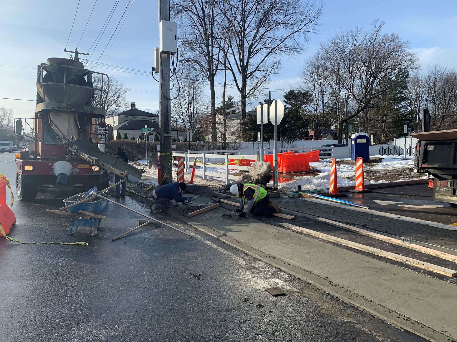 Concrete being poured from a truck onto a road as workers apply the wet concrete.