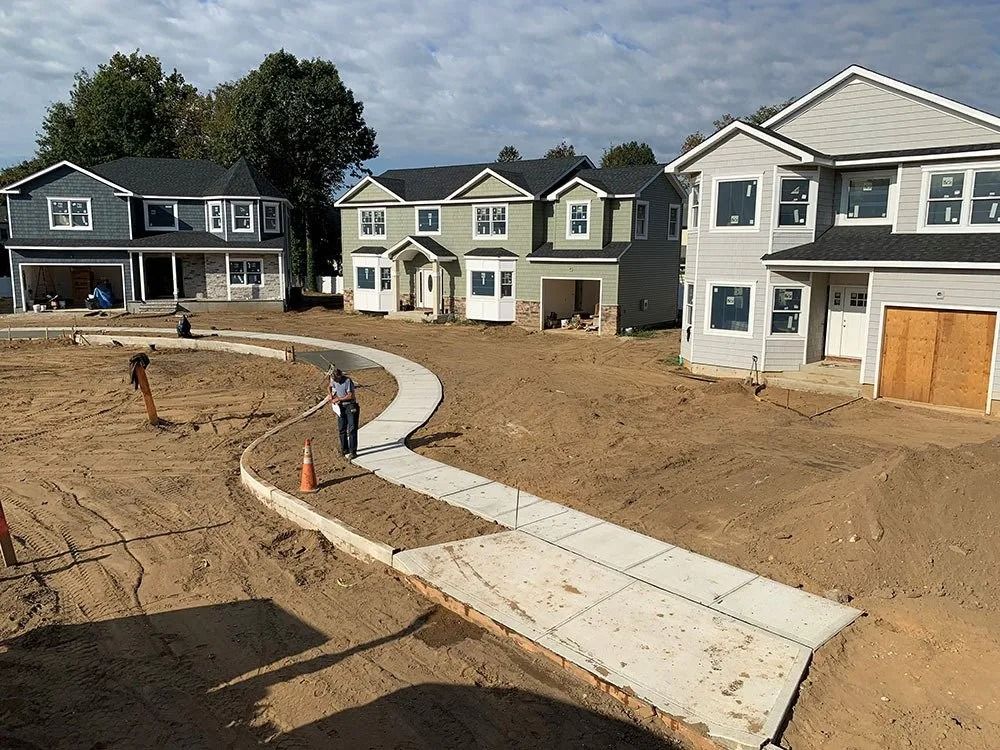 Construction site with three newly built houses and a concrete sidewalk.