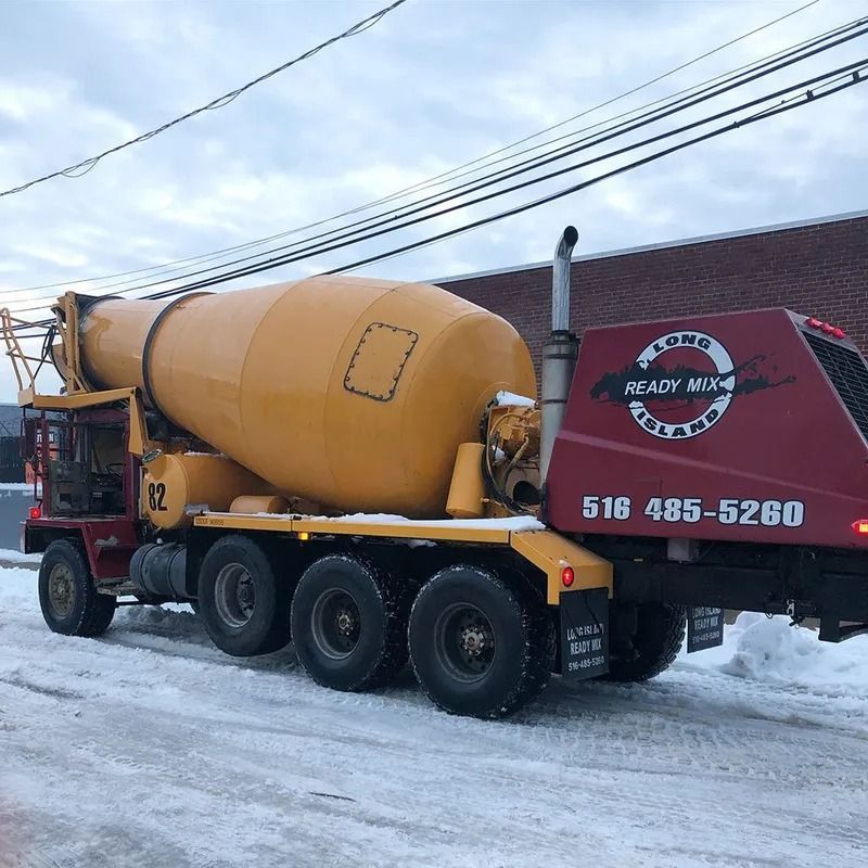 Yellow cement truck on snowy road, ready mix logo on red rear.