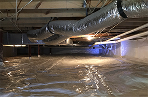 The ceiling of a basement is covered in plastic and ducts are hanging from the ceiling.