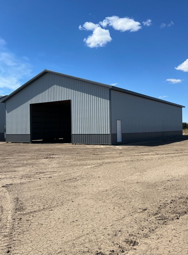 A large metal building with a black door is sitting in the middle of a dirt field.