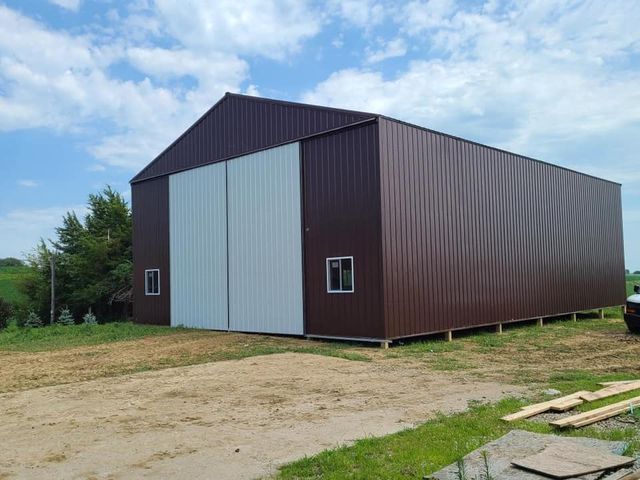 A large brown barn with a white door is sitting in the middle of a dirt field.