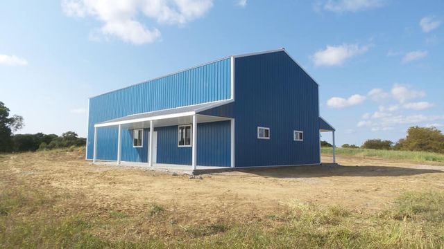 A blue building with a porch is sitting in the middle of a field.