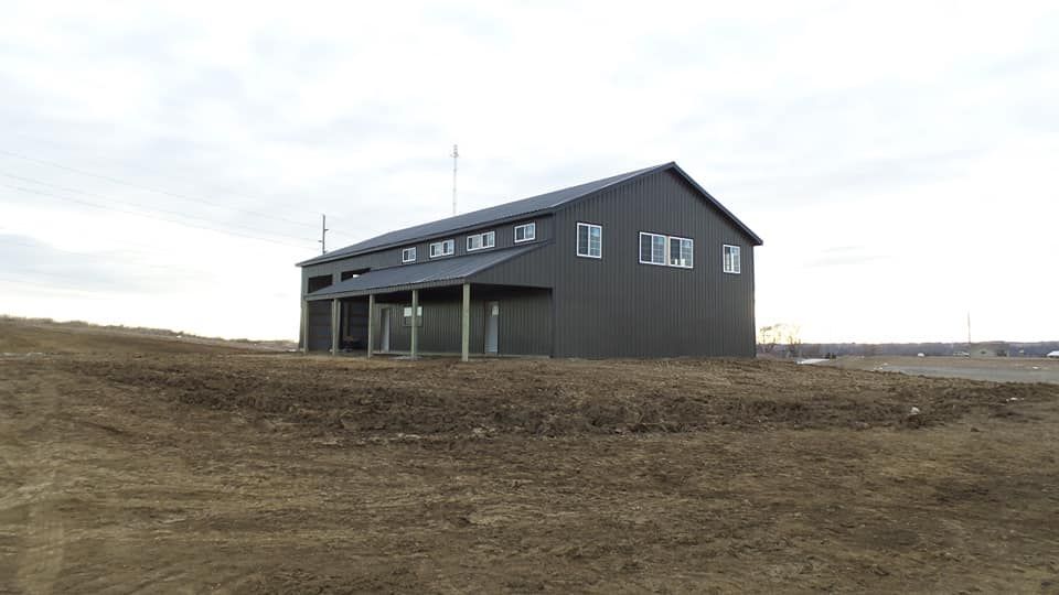 A large black barn is sitting on top of a dirt field.