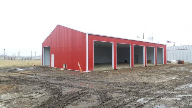 A large red barn is sitting in the middle of a dirt field.