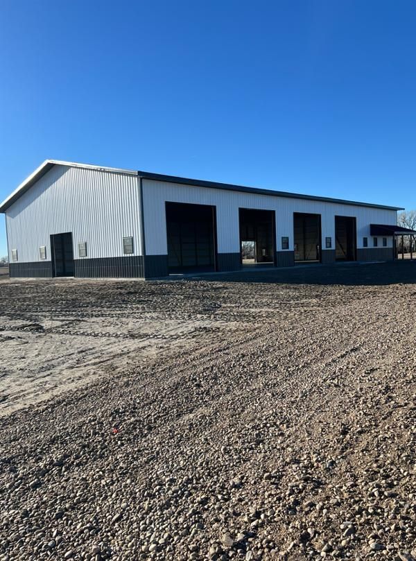 A large white building with black trim is sitting on top of a gravel road.