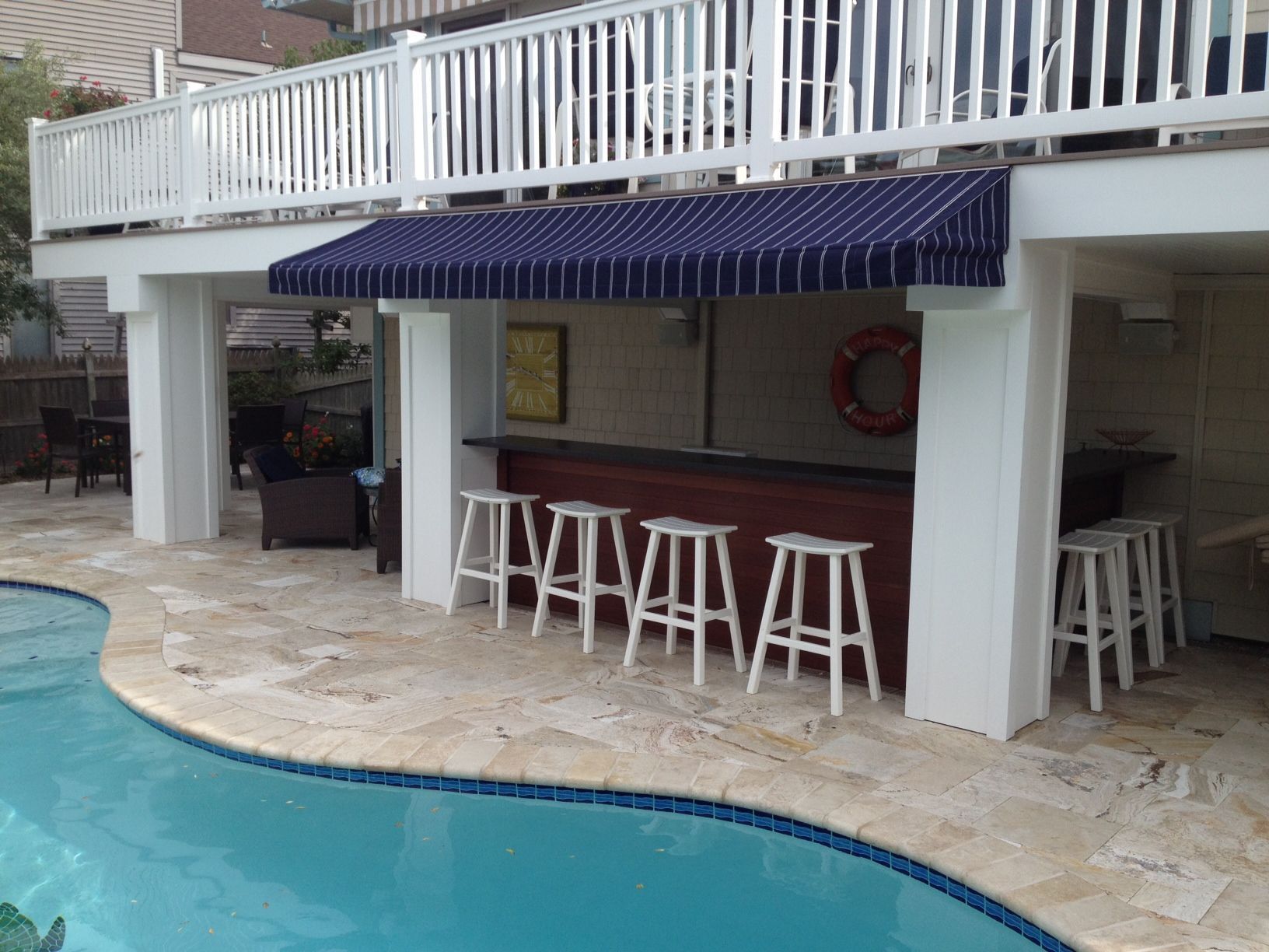 Poolside bar with a blue and white striped awning and white bar stools.