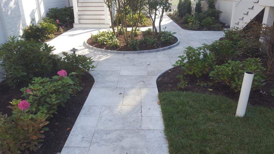 Stone walkway curves through landscaped garden with greenery and flowers.