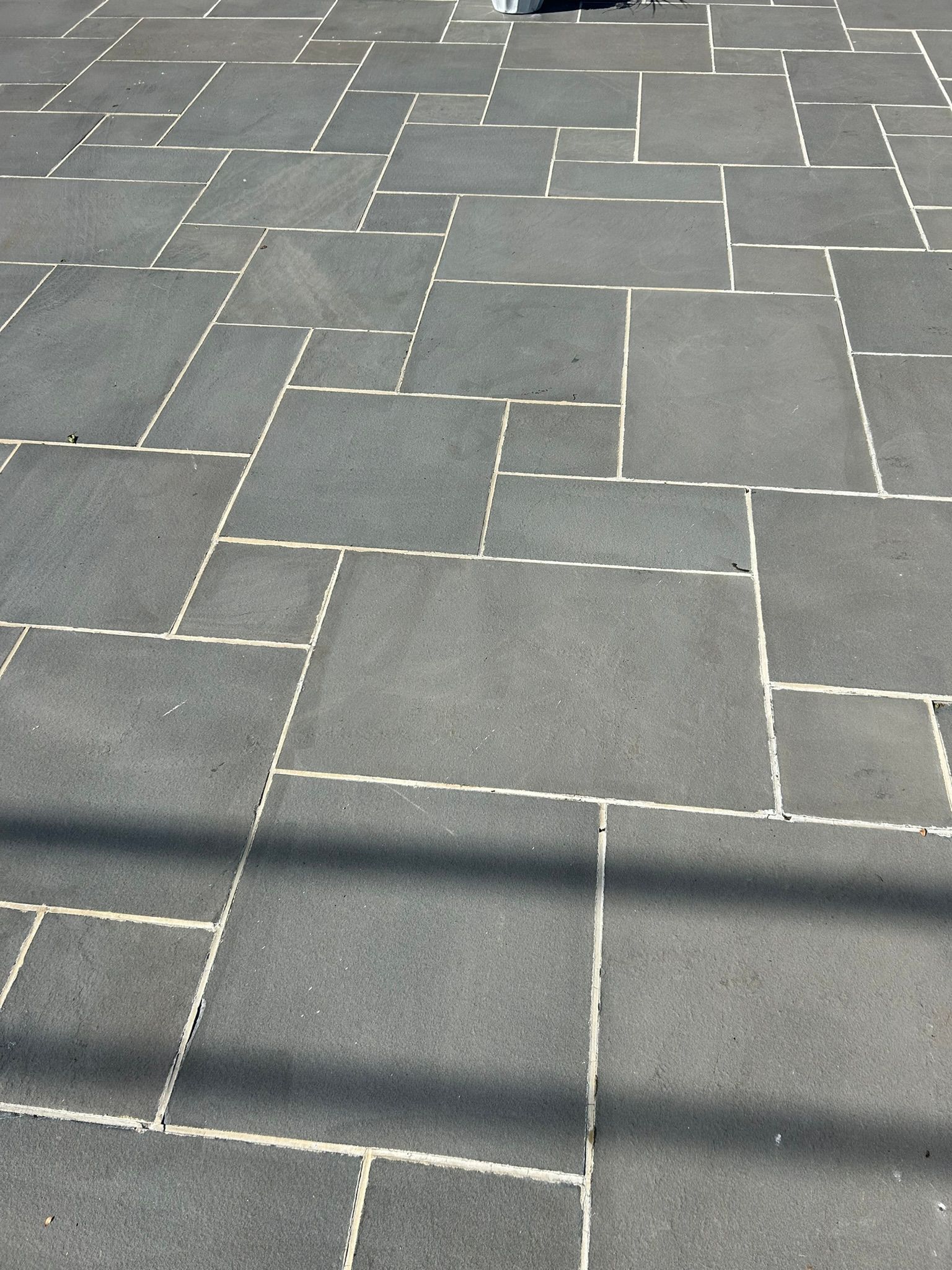 Dark gray stone pavers with white grout lines creating a geometric pattern on a walkway.