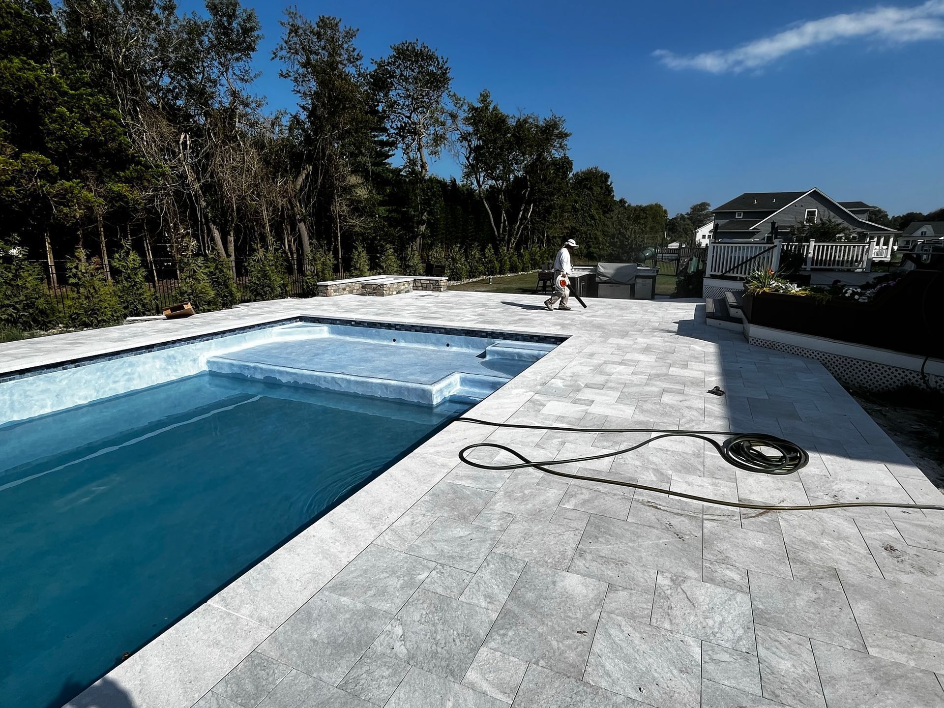 Pool and patio with worker. Blue water, light stone patio, sunny day.