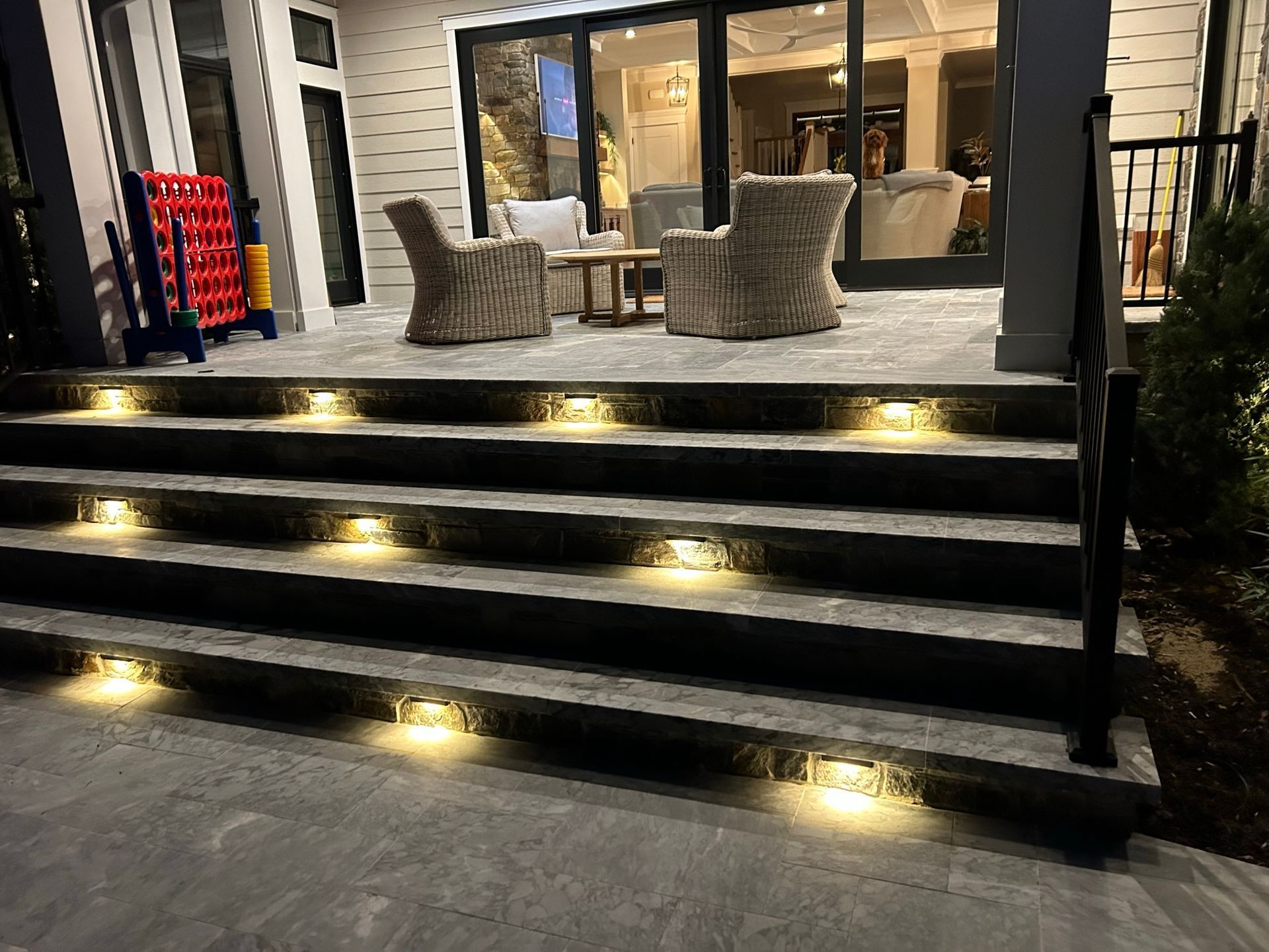 Outdoor stone steps with built-in lights, leading to a patio with wicker chairs and a table.