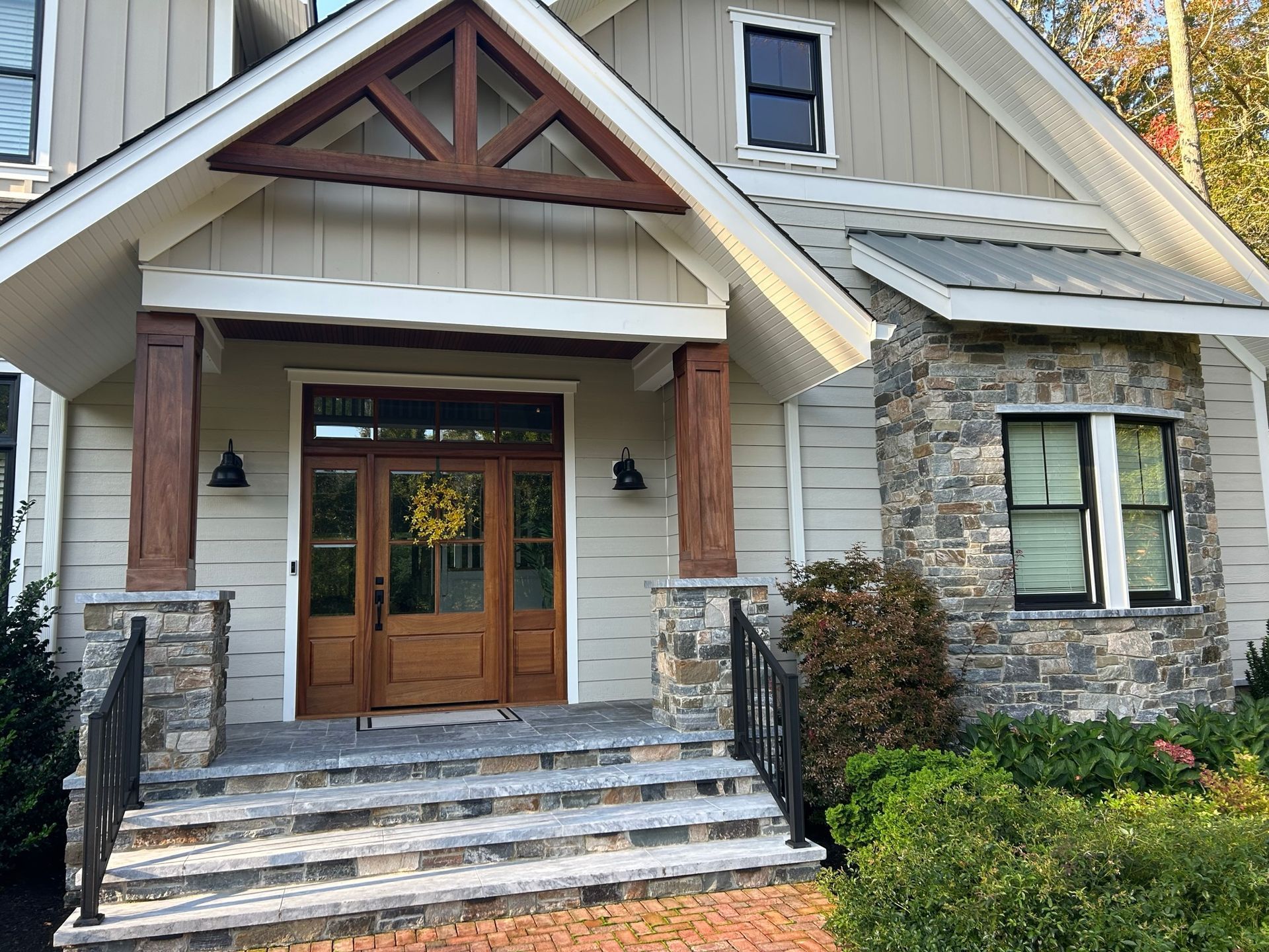 Beige house with stone accents, wooden door, steps, and black iron railing.
