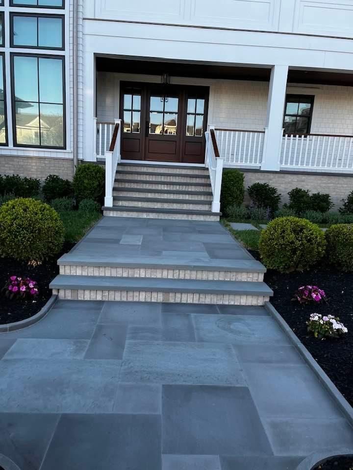 Stone walkway and steps leading to a house with white siding and dark wooden doors.