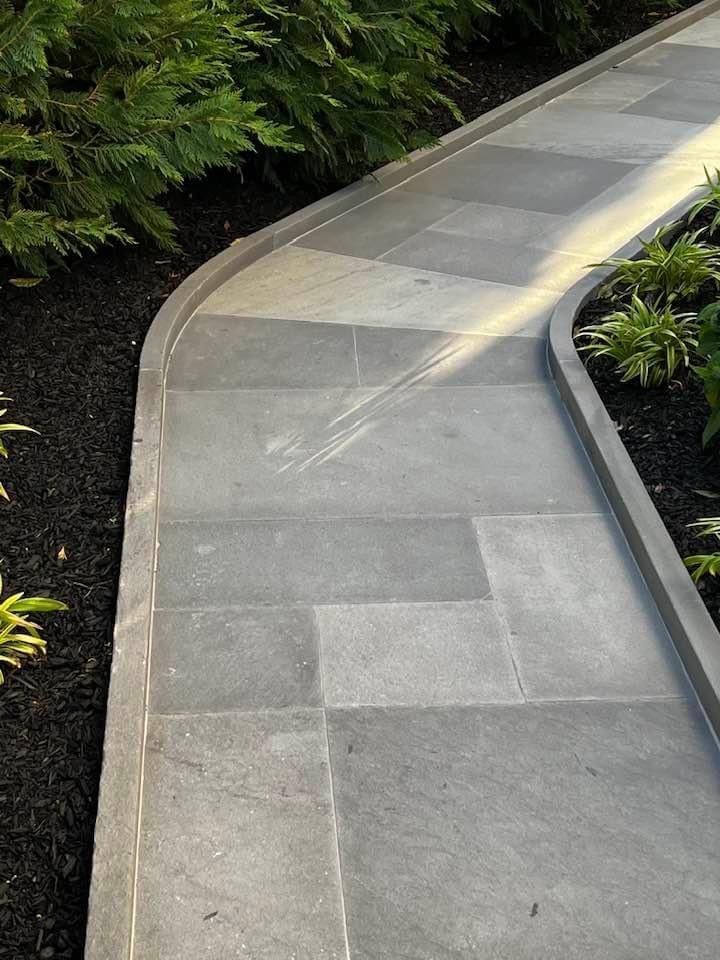 Curving stone walkway with dark mulch border, edged by greenery.
