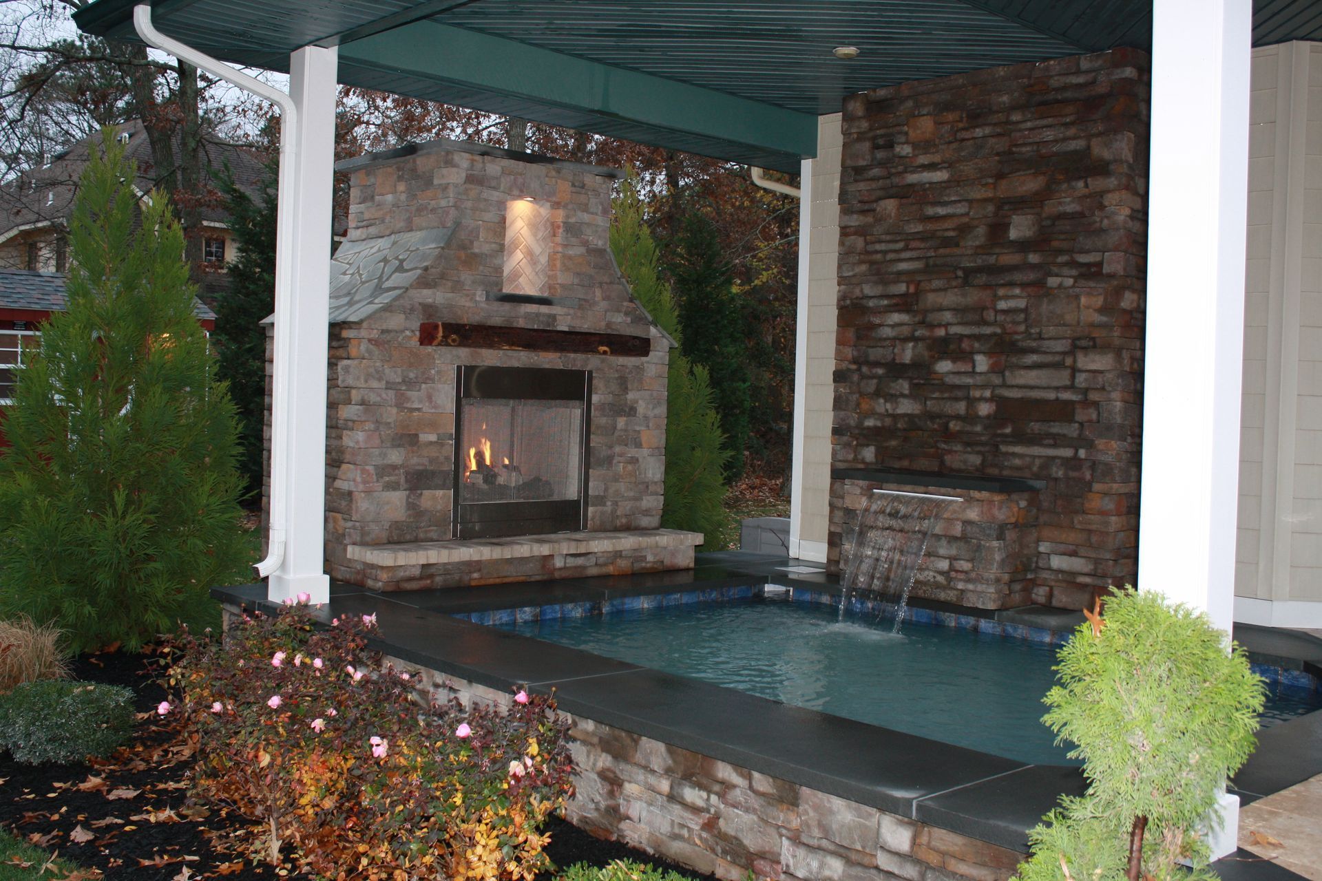 Outdoor fireplace and small pool with stone facade under a covered patio.