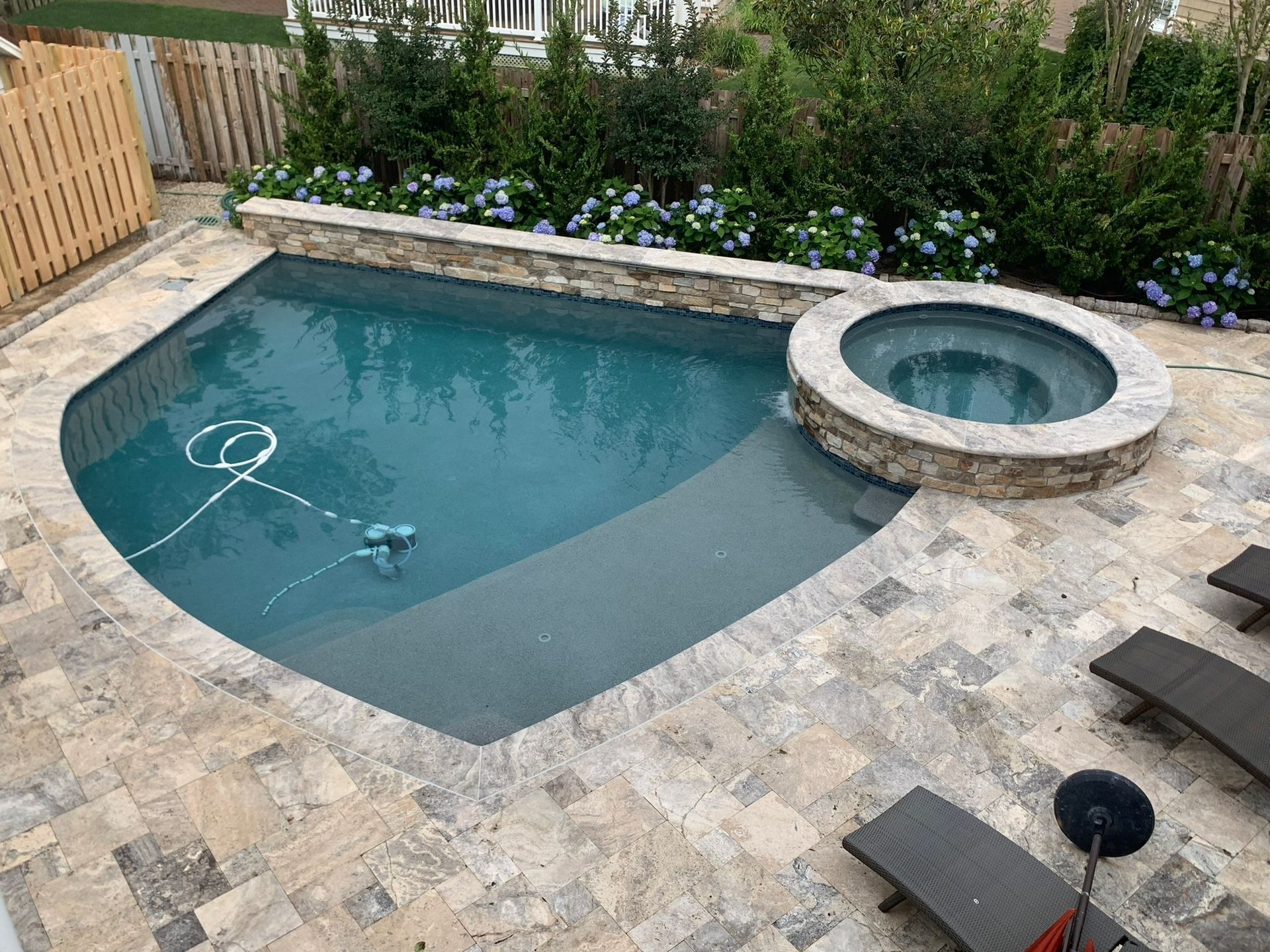 Backyard pool with spa, stone deck, and blue hydrangeas.