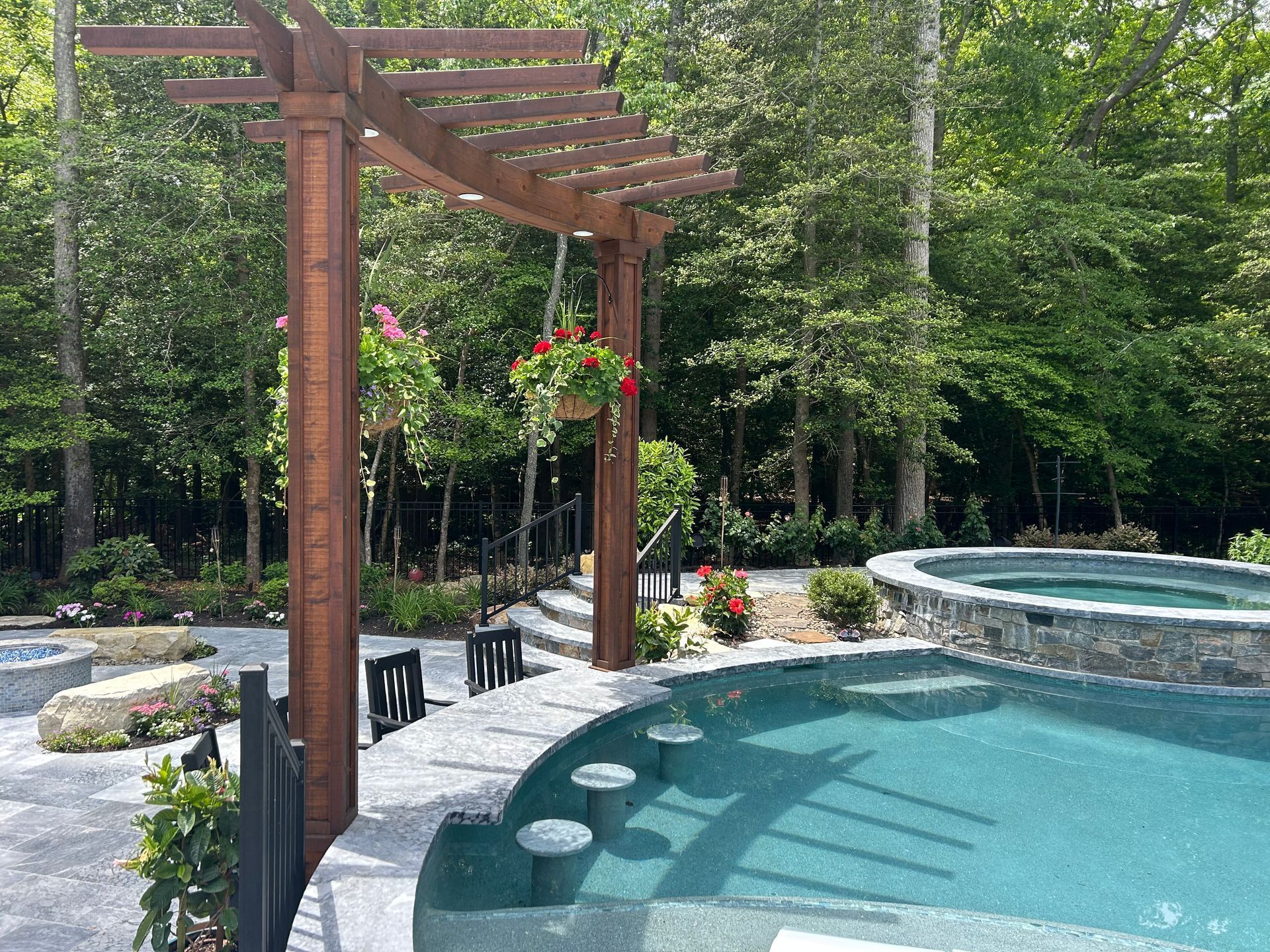 Pergola over pool with a hanging basket, surrounded by trees.