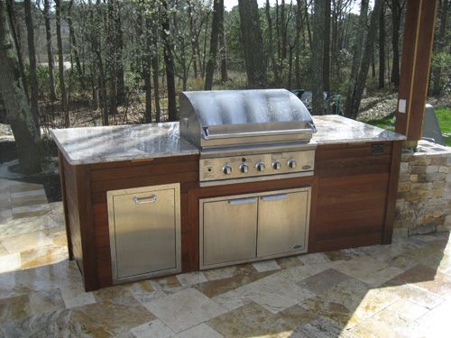 Outdoor kitchen with stainless steel grill, cabinets, and stone countertop on a stone patio.