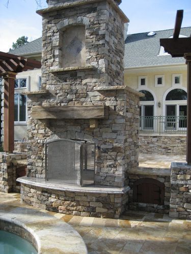 Stone outdoor fireplace with chimney, built-in features, and wooden beam.