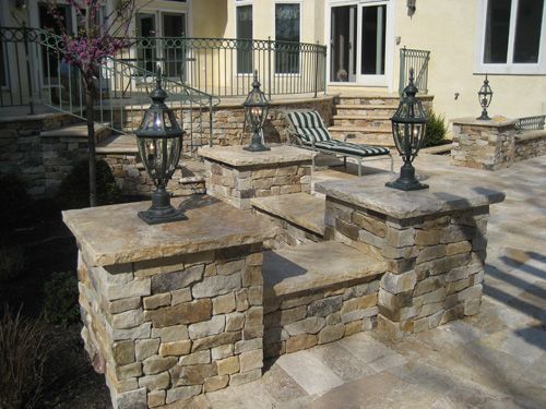 Stone steps with decorative lamps on a patio next to a house with a lounge chair.