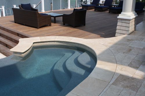 Pool with steps and deck with furniture; sunny outdoor setting.