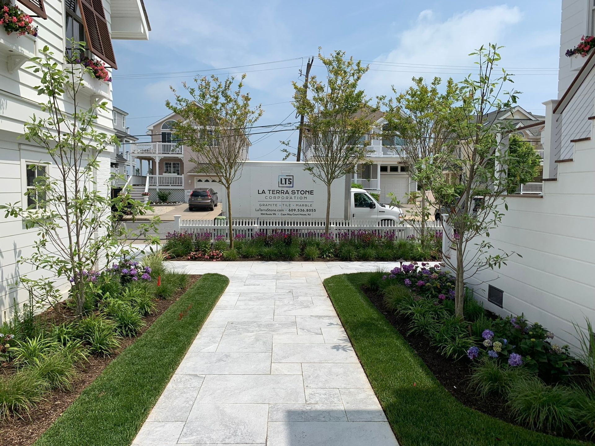 Pathway through landscaped garden towards houses. White truck parked in the background.