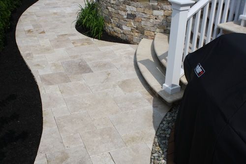 Curving stone walkway leading to steps and white railing. Grill cover on the right.