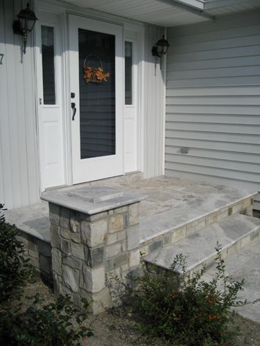 Front entrance with stone steps and pillar leading to a white door with sidelights.