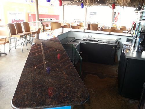 Outdoor bar with granite countertop, chairs, and thatched roof.