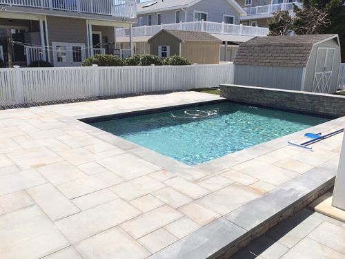 Pool with blue water and stone patio surrounded by a white fence and beach houses.