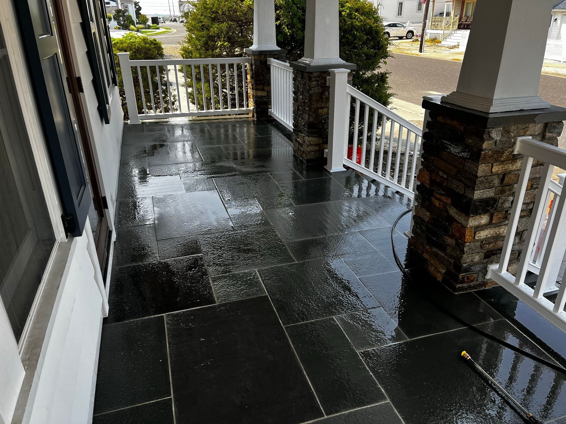 Wet, dark stone porch with white railing and columns. Street view.