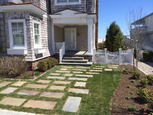Stone pathway leads to a house with a small white picket fence and a covered porch.